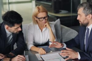 Tres personas en reunión de negocios analizando gráficos y tomando notas sobre la mesa.